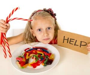 Little girl sitting in front of candy bowl with help sign 