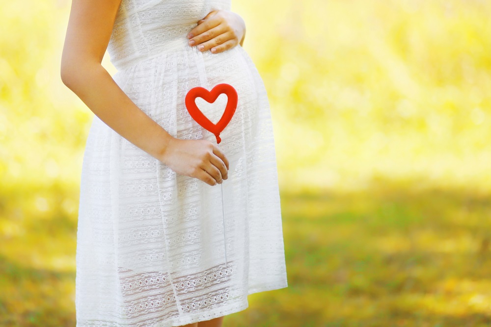 pregnant woman holding heart prop over her belly
