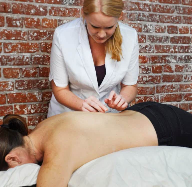 Dr. Erin performing an acupuncture treatment on client on table